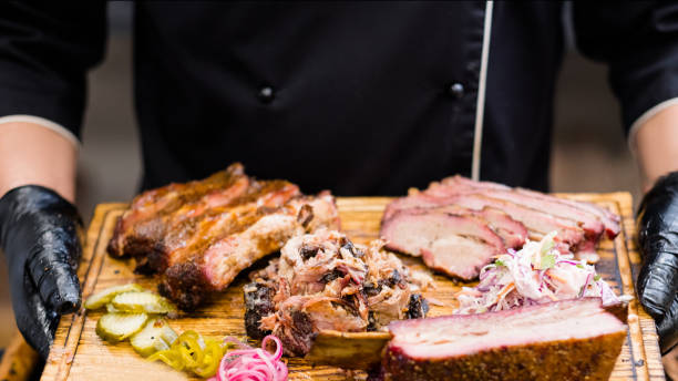 food delivery service smoked meat assortment Food delivery service. Cropped shot of chef holding wooden board with smoked meat assortment, coleslaw salad, pickles. smoked food stock pictures, royalty-free photos & images