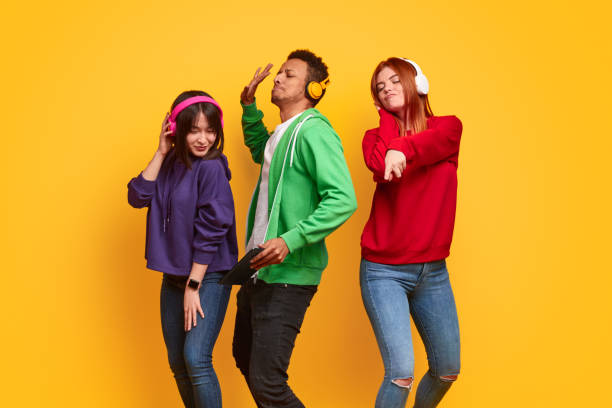 Mutliethnic friends in headphones dancing Group of multiracial students with closed eyes listening to music in headphones and dancing together against bright yellow background asian man headphones stock pictures, royalty-free photos & images