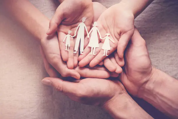 Photo of Adult and children hands holding paper family cutout, family home, foster care, homeless charity support concept