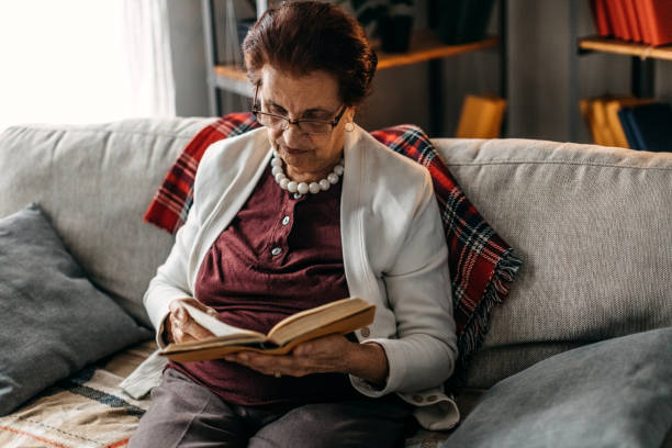 istock Old woman sitting on sofa and reading a book 1169663895