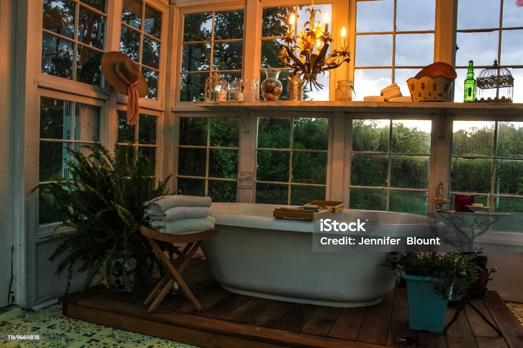 Interior of a greenhouse with a large soaking tub on a wooden platform with a tole chandelier plants towels and a stenciled floor Bathroom Stock Photo