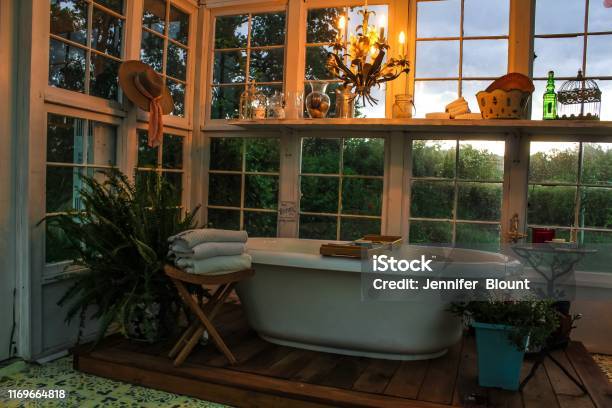 Interior Of A Greenhouse With A Large Soaking Tub On A Wooden Platform With A Tole Chandelier Plants Towels And A Stenciled Floor Stock Photo - Download Image Now