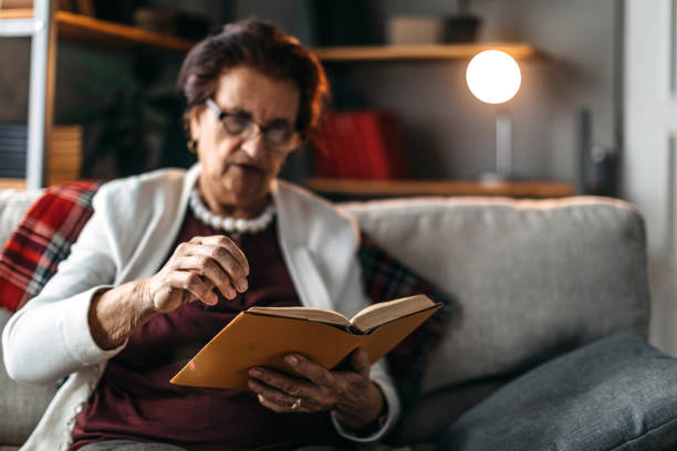 istock Old woman sitting on sofa and reading a book 1169666639