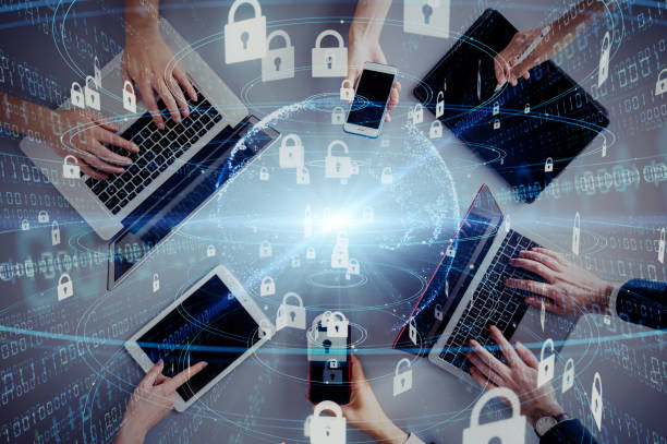 Aerial view of multiple hands interacting with digital devices, including laptops, tablets, and smartphones, surrounded by a glowing globe and floating padlock icons symbolizing cybersecurity and data protection.