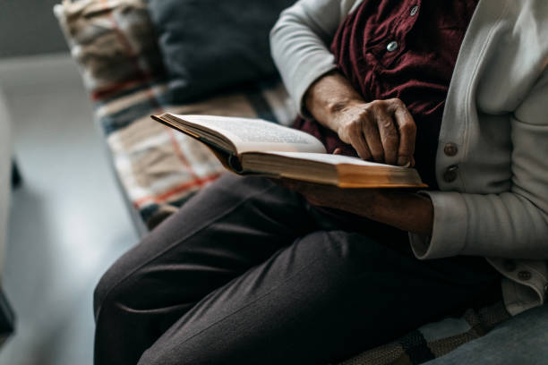 istock Old woman sitting on sofa and reading a book 1169668447