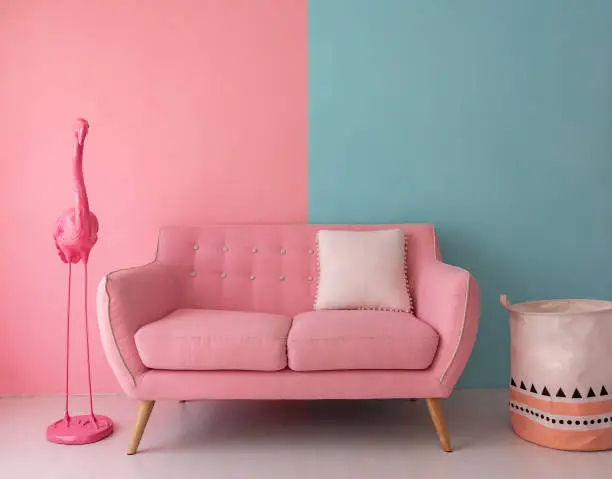 The pink sofa which has a white pillow is set in living room which has blue and pink wall.