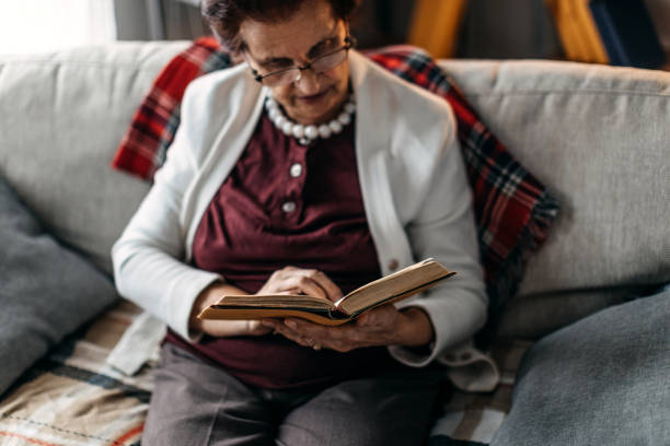 istock Old woman sitting on sofa and reading a book 1169676062