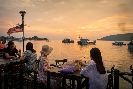 Two women vacationing from Korea enjoy a sunset drink at the waterfront, a public walkway lined with restaurants in Kota Kinabalu, Sabah, Malaysia. (August 14, 2019)