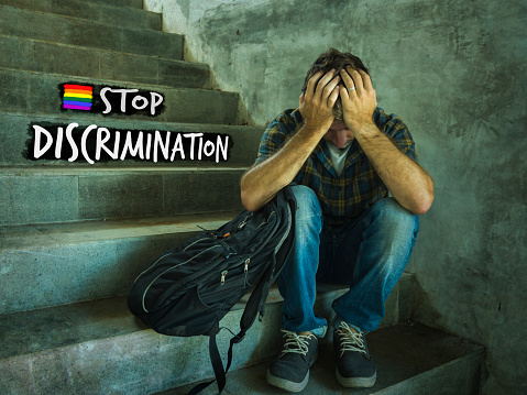 free sexual orientation and LGBT tolerance and respect campaign with young harassed and bullied homosexual student man sitting on staircase victim of bullying and abuse