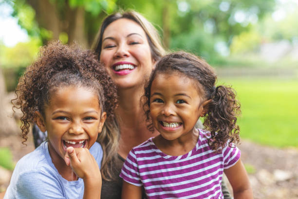 Asian Chinese Mother with two daughters of mixed Chinese and African American ethnicity in a green lush back yard setting posing for portraits smiling and being silly stock photo