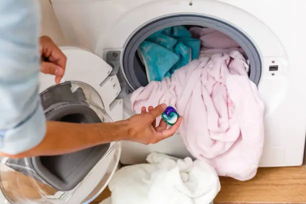 Photo of blue gel caps in hand for washing mashine, liquid coloured detergent