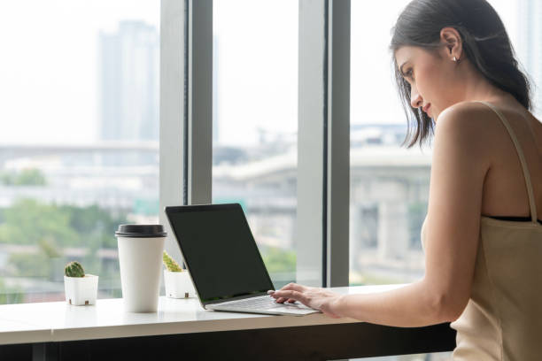 istock Young business woman using laptop computer while sitting at cafe table next to office windows. 1169700518