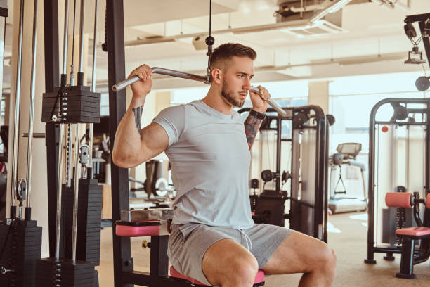 istock Young tattoed man is doing exercise for back on training apparatus in gym 1169704062
