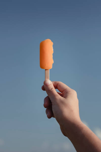 mãos da mulher que prendem o gelado de derretimento alaranjado sherbet o fundo do dia ensolarado da luz natural do verão. põr sua mão colocada ao céu azul - arms raised people orange blue - fotografias e filmes do acervo