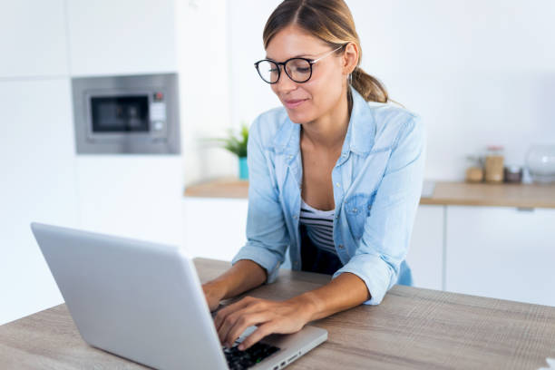 istock Pretty young woman using her laptop in the kitchen at home. 1169718898