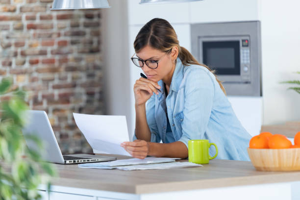 istock Pretty young woman working with laptop and documents in the kitchen at home. 1169718983