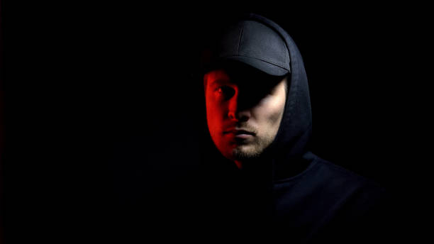 istock Man in cap and hoodie looking at camera, red light, police raid, catching thief 1169728836
