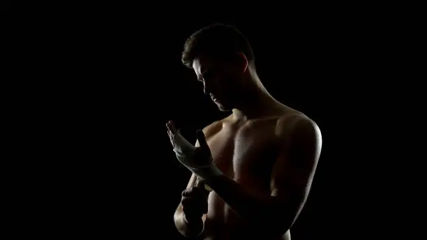 Photo of Male boxer using hand wraps, protecting wrists from injuries before punching