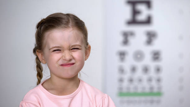 ragazza carina che rovina gli occhi, cercando di vedere le lettere sul tavolo per il test della vista - strizzare gli occhi foto e immagini stock