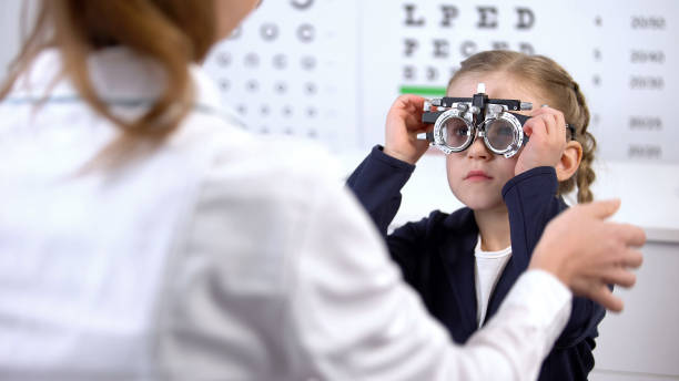 jolie petite écolière visitant oculist pour mesurer la vue avec le phoropter - examen ophtalmologique photos et images de collection