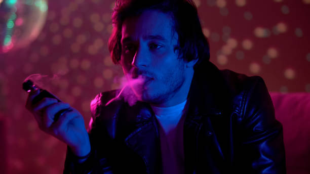 pensive guy vaping electronic cigarette in club, nicotine smoke harming health - harming imagens e fotografias de stock