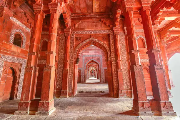 Fatehpur Sikri Agra red sandstone medieval architecture with Mughal wall art carving and architectural columns of the 16th century. View of the hall leading out to the courtyard of Fatehpur Sikri historic fort city at Agra, India