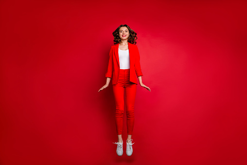 Full length photo of cute girl jumping, looking isolated over red background
