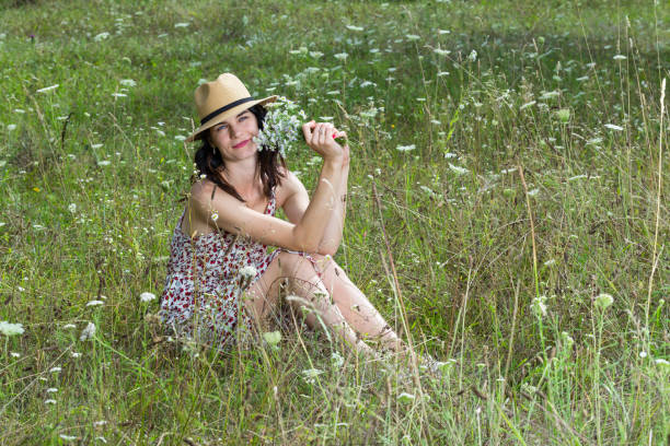 Beautiful woman sits in a field with flowers in her hands.