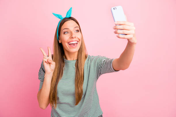 istock Funny lady making selfies with v-sign symbol wear striped pullover isolated pink background 1169749974