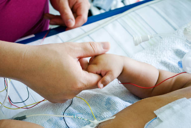 a mother's hand comforting a critically sick baby hooked on a ventilator in a hospital paediatric intensive care ward - nurse illness doctor heart disease imagens e fotografias de stock