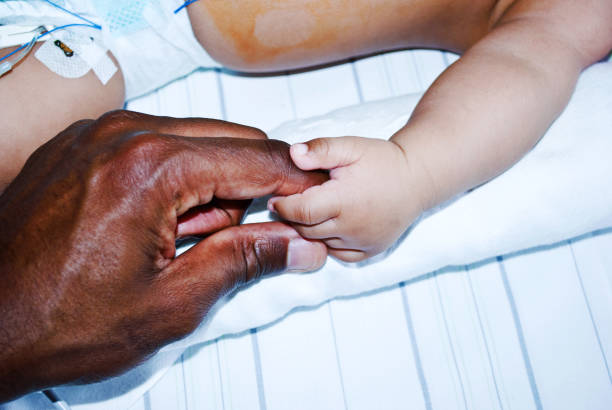 a hand comforting a critically sick baby hooked on a ventilator in a hospital paediatric intensive care ward - nurse illness doctor heart disease imagens e fotografias de stock