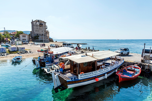 Ouranoupoli-Athos, Greece - August 19, 2019: Boats organizing touristic tour to various regions from Ouranoupoli harbor and Byzantine Tower in Athos peninsula, Halkidiki, Greece.