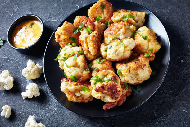 Fried in batter Cauliflower florets served on a black plate Cauliflower florets fried in batter served on a black plate on a grey concrete table, view from above, close-up breaded photos stock pictures, royalty-free photos & images