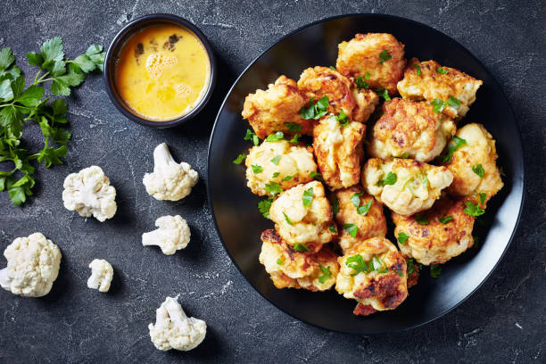 fritos en masa floretes de coliflor servidos en un plato negro - cauliflower roasted parsley cooked fotografías e imágenes de stock