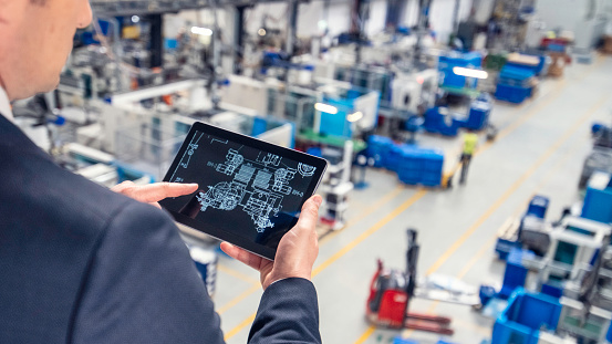 Photo of a man using a digital tablet with a schematic in a factory.