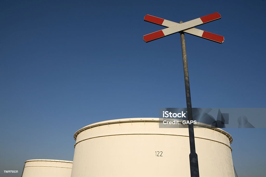 railroad crossing close to storage tanks of an oil refinery railroad crossing sign close to the fuel storage tanks of an oil refinery Air Pollution Stock Photo