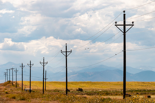 Power lines recede into the distance in Colorado with Rocky Mountains in the background.
