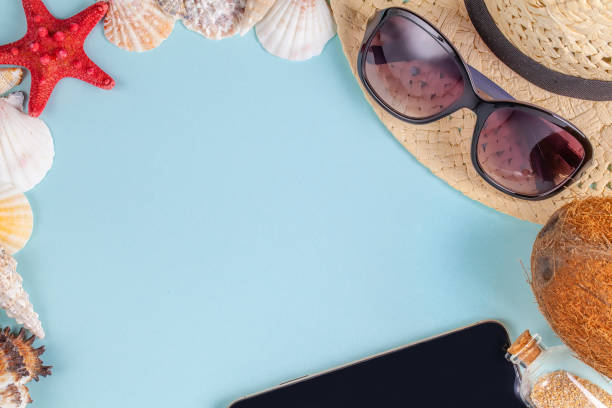 istock Sunglasses, coconut, starfish, shells, straw hat, bottle with sand and mobile phone on blue background 1169760065