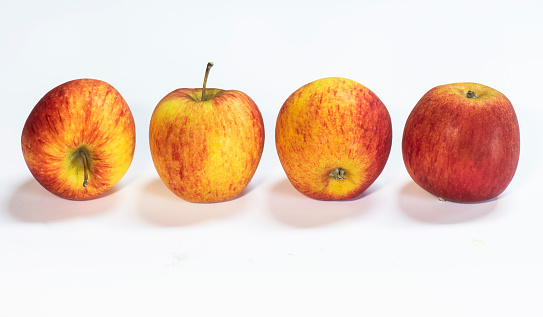 a row of equally spaced fresh apples at different angles on a white background complete with shadows