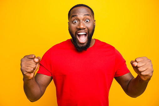 Photo of excited crazy, black man having possibly won some contests end rejoicing with it while isolated with yellow background