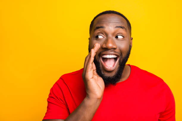 Close up photo of cheerful positive playful man telling someone secrets of him announcing important information while isolated with yellow background Close up photo of cheerful, positive playful man telling someone secrets of him announcing important information while isolated with yellow background whisper men stock pictures, royalty-free photos & images