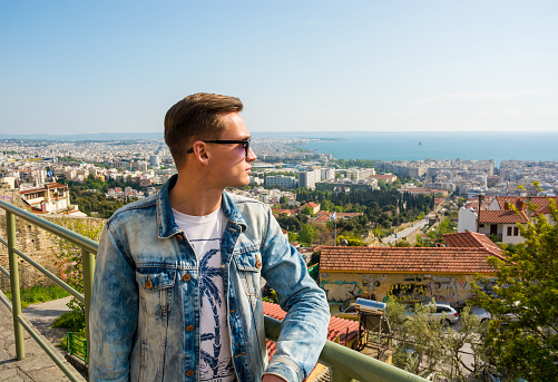 Young handsome man, tourist, near the Upper Town Fortress in the Ano Poli, Thessaloniki, Greece. View of the sea in the Ano Poli