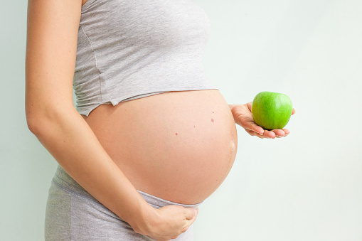 pregnant girl holding a green apple.pregnant girl holding a green apple. nutrition during pregnancy. Vitamins and pregnancy. Source of iron, pregnant anemia. Vegetarianism and pregnancy.