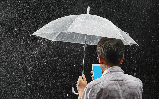 Middle aged asian male holding his umbrella and phone under rain in night time