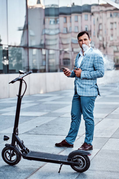 Elegant man with electro scooter is smoking vape