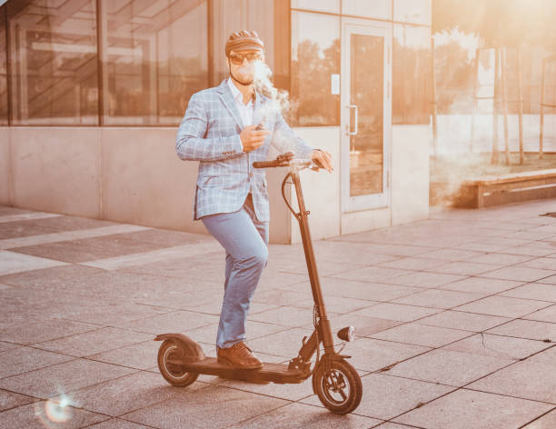Elegant man with electro scooter is smoking vape