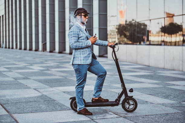 istock Elegant man with electro scooter is smoking vape 1169781491