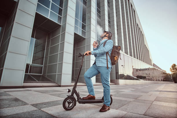 istock Elegant man with electro scooter is smoking vape 1169783842