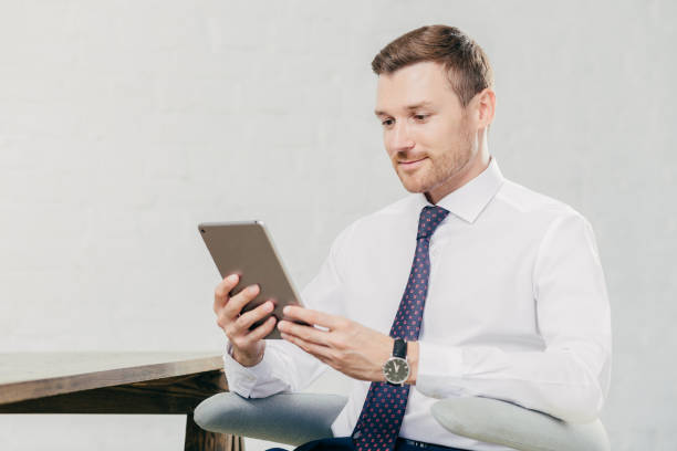 istock Male executive manager in white shirt and tie, holds tablet computer, searches necessary information in internet, connected to wifi in office. People, business and modern technologies concept 1169787050