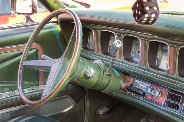 Photo of Green leather, wood and chrome interior of a classic american luxury oldtimer car. Steering wheel, radio, speedometer and a hairy dice